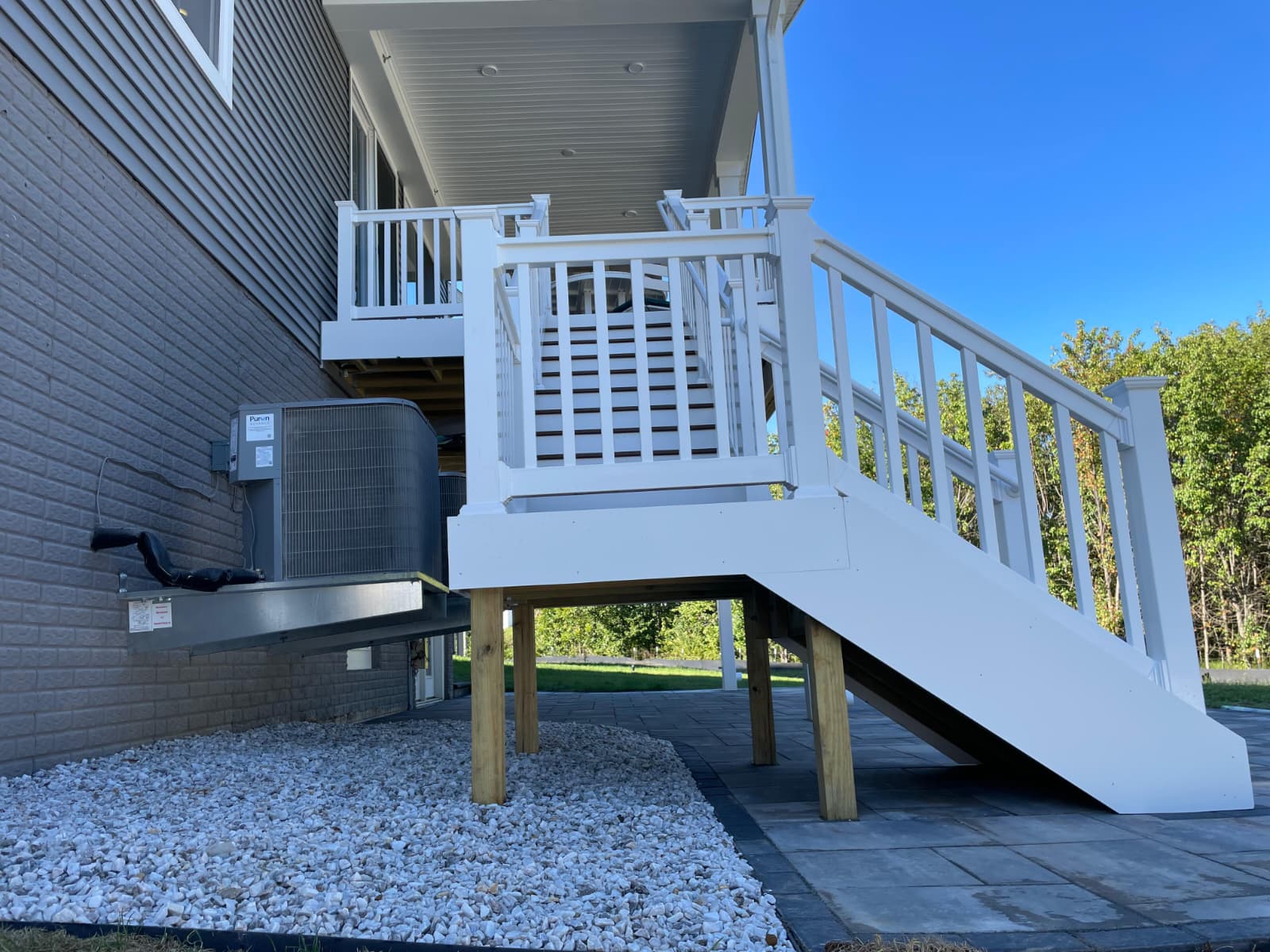 White deck stairs with stone patio and river rock base